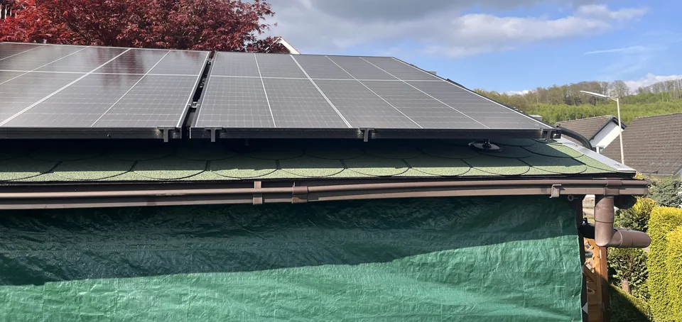 Solarmodule auf einem flach geneigten Dach über einer grünen Abdeckung.