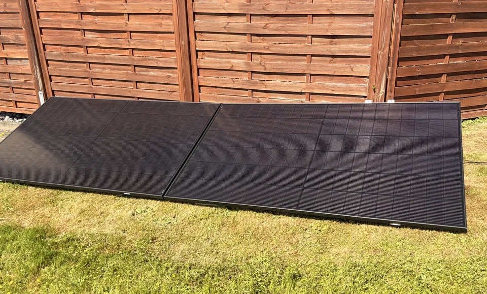 Zwei schräg aufgestellte Solarmodule auf einer Rasenfläche vor einem Holzzaun.